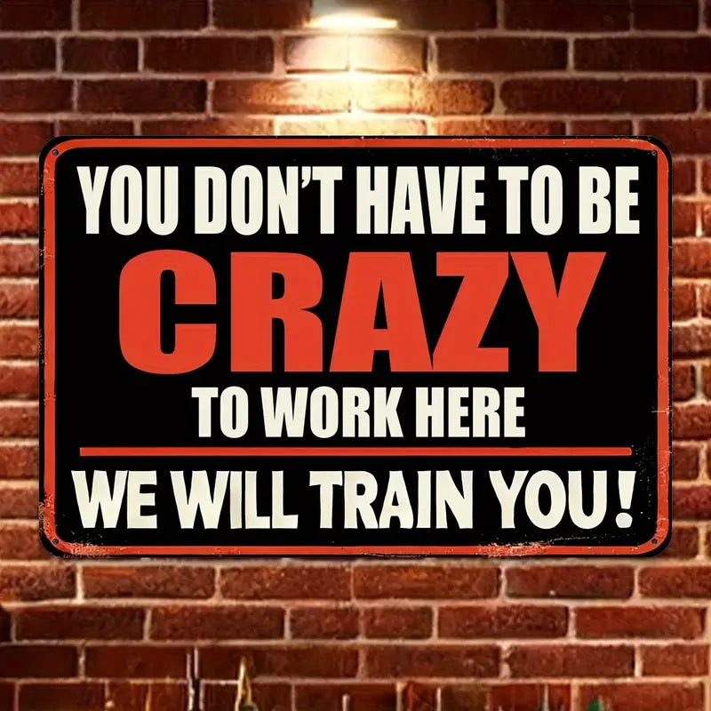 Motivational sign on a brick wall reading 'You don't have to be crazy to work here. We will train you!'