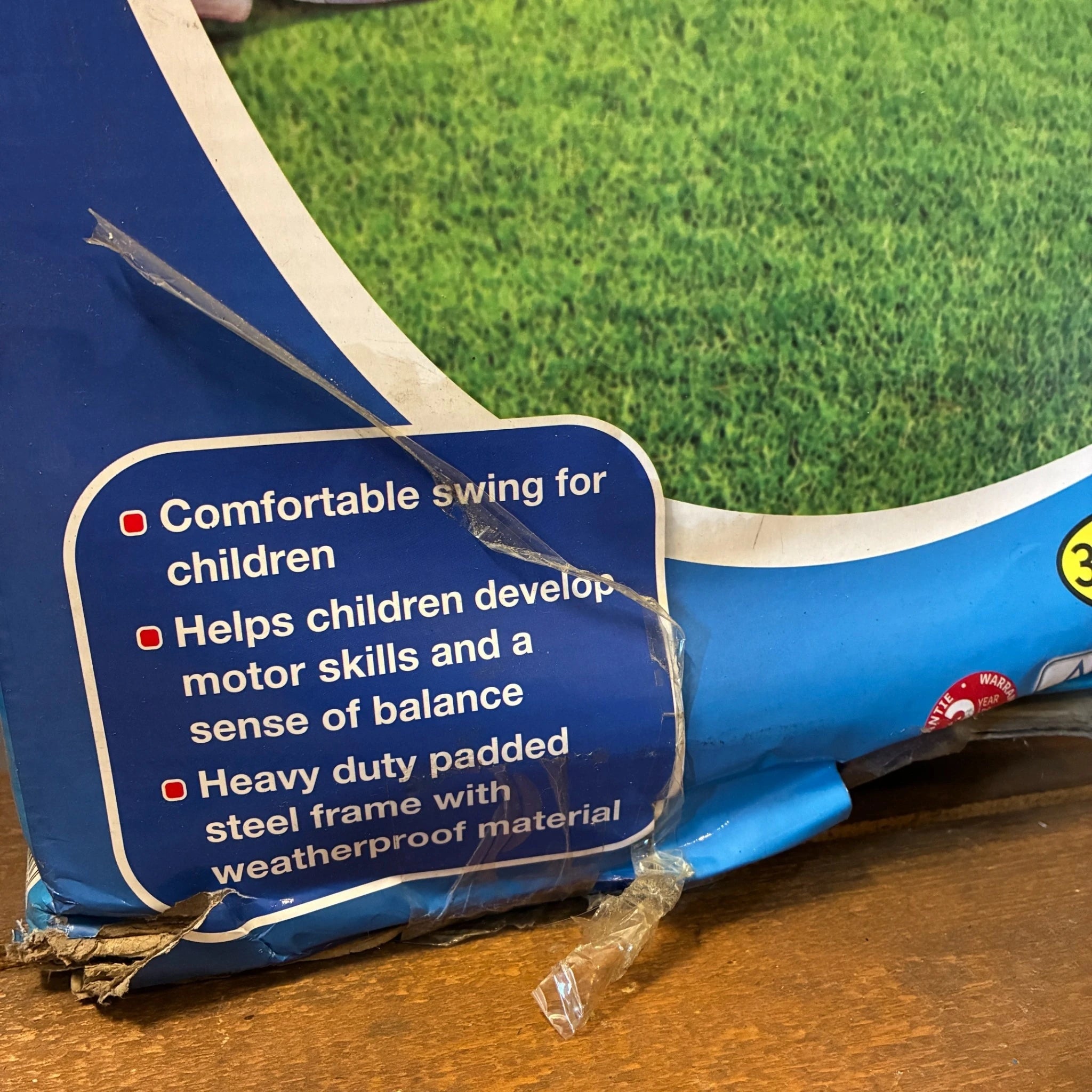 Blue swing set with safety label on grass and wooden floor