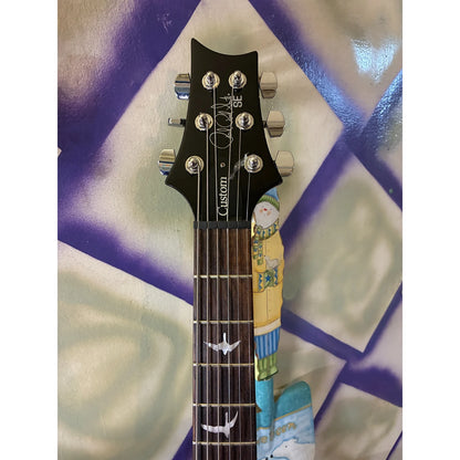 Close-up of a guitar headstock and upper fretboard. The headstock is black with silver tuning pegs and a visible 'CANTON' logo, while the fretboard is dark wood with white bird inlays.