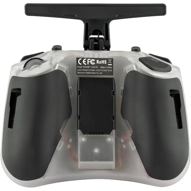 A close-up of a remote control transmitter with a transparent casing, black grips, and a black top handle, showing a central battery compartment and regulatory labels.